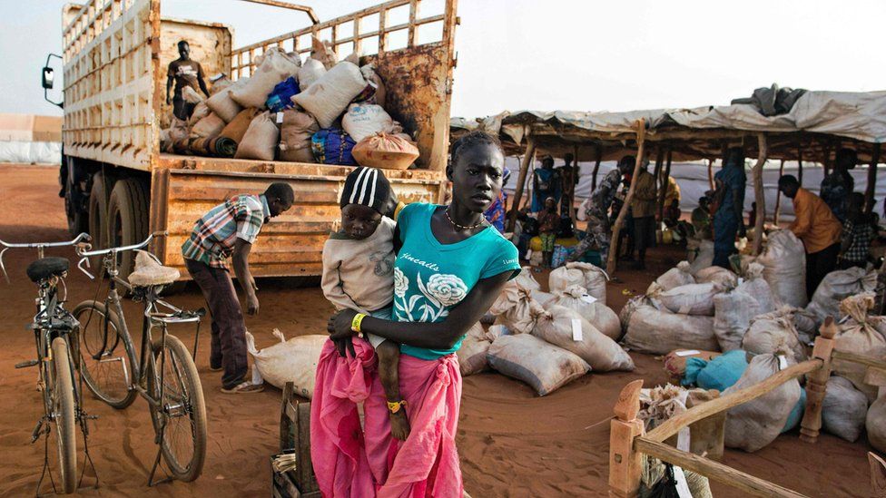 An asylum seeker and her baby from Sudan, who recently arrived in South Sudan, stands beside a truck holding some of her belongings before she is transferred to the refugee camp in Ajuong Thok, near Yida, northern South Sudan