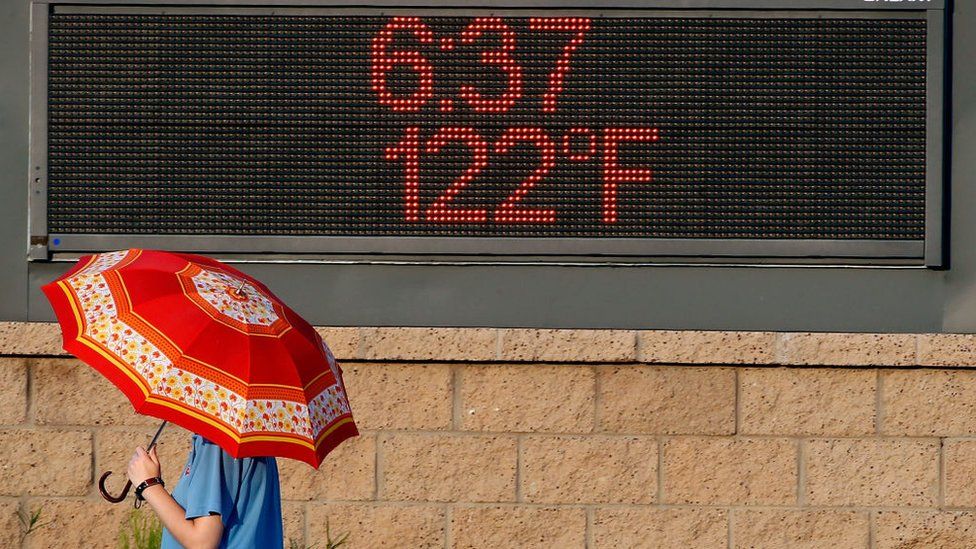 A pedestrian uses an umbrella to get some relief from the sun as she walks past a sign displaying the temperature on June 20, 2017 in Phoenix, Arizona