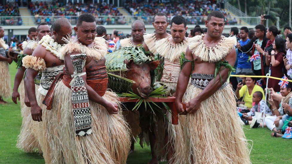 Men in traditional attire carry a roasted pig