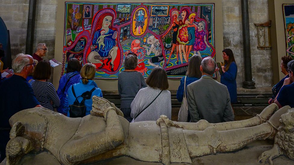 Visitors to the cathedral observing the colourful tapestry, stood in front of a tomb monument