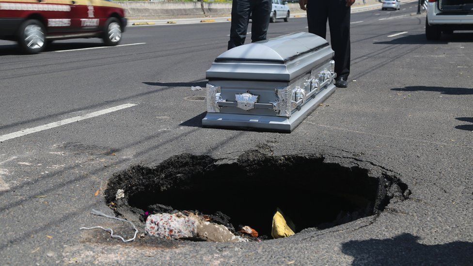 A coffin is placed next to a pothole in Mexico City