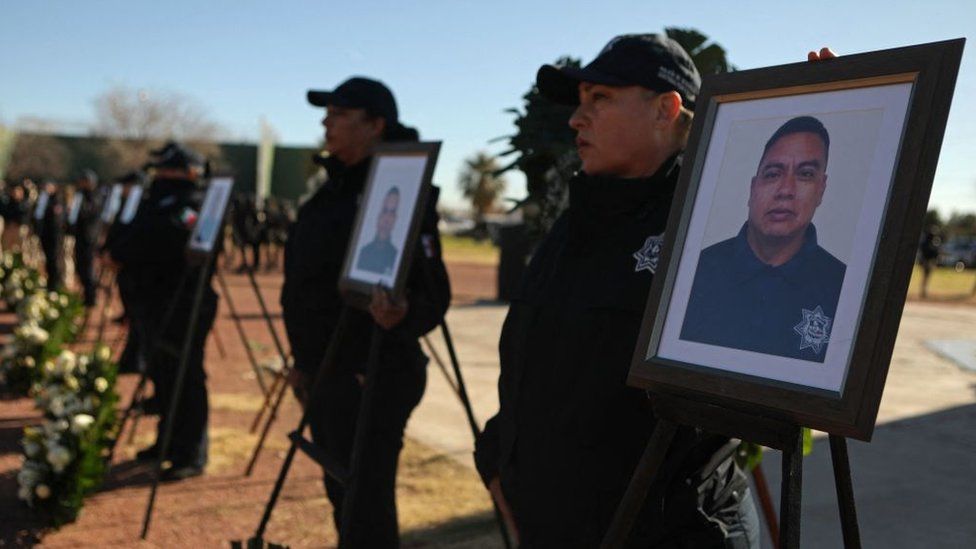 Агенты службы безопасности стоят рядом с фотографиями тюремных охранников, погибших в результате нападения на тюрьму в Сьюдад-Хуаресе, Мексика