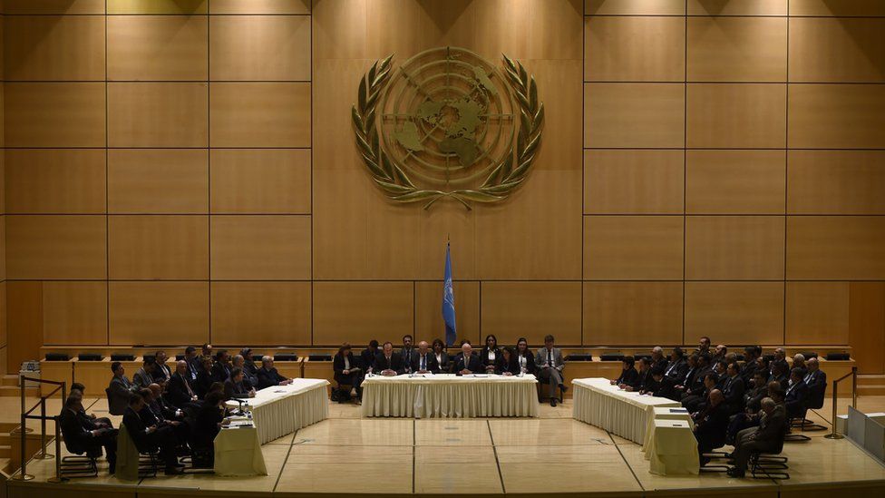 The assembled delegates face each other across a grand chamber, beneath the United Nations symbol