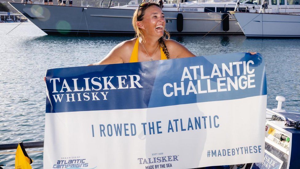 Atlantic rower Lara Vafiadis holds up a banner