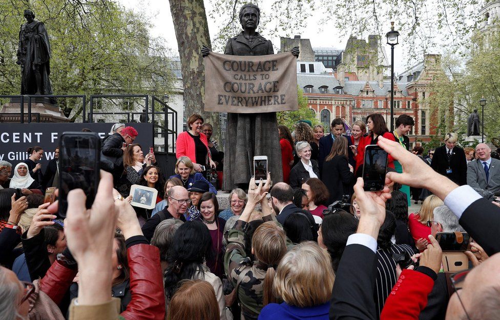 People pose for photographs with a statue of suffragist and women's rights campaigner Millicent Fawcett