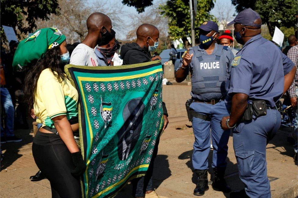Полиция трогает вооруженных флагом сторонников бывшего президента ЮАР Джейкоба Зумы, которые протестовали перед Высоким судом в Питермарицбурге, ЮАР, 6 июля 2021 г.