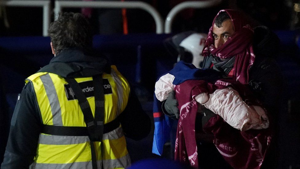 A man carries a baby as a group of people thought to be migrants are brought in to Dover, Kent,