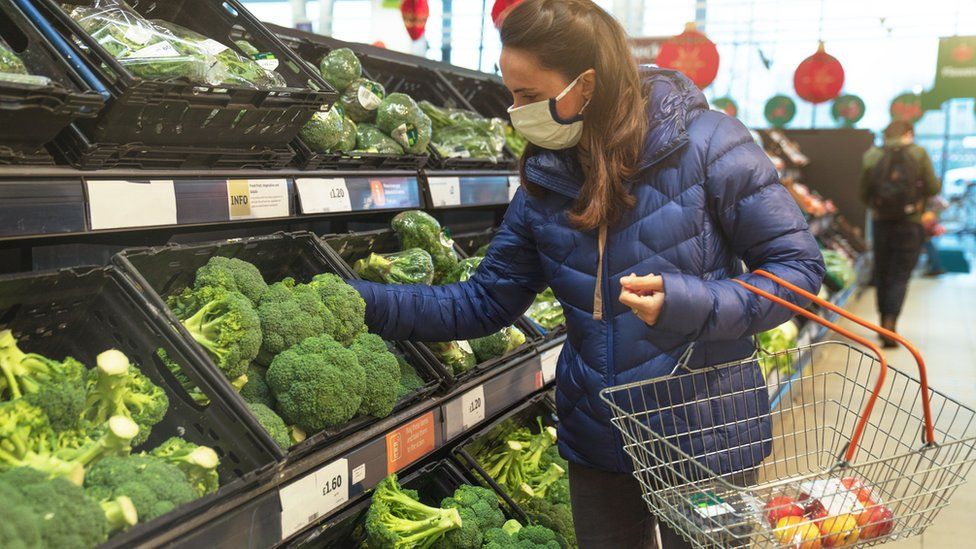 Woman wearing protective face mask doing grocery shopping for fresh vegetables in supermarket.