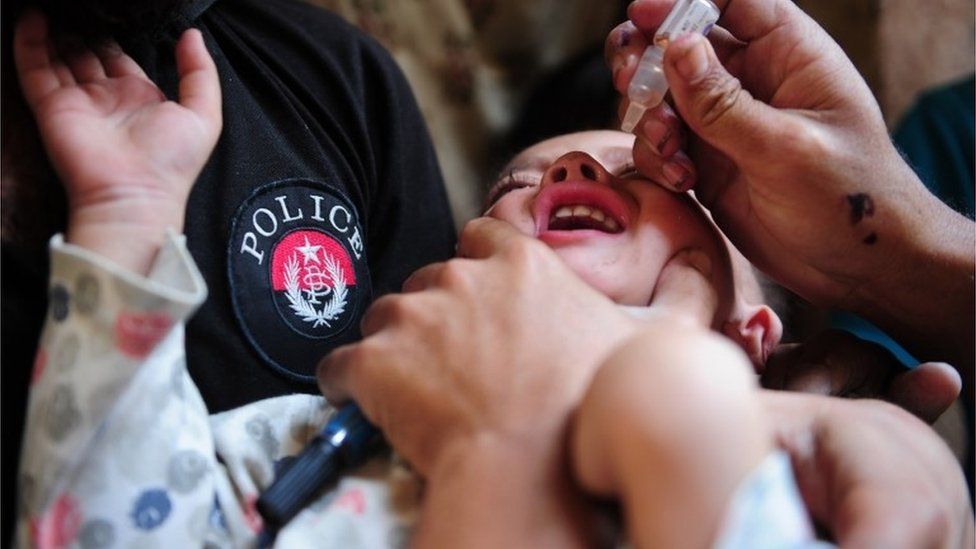 A Pakistani policeman holds a young girl as a health worker administers polio drops during a polio vaccination campaign in Karachi on January 11, 2016