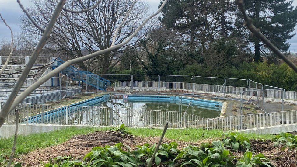 Broomhill Lido, cordoned off by metal fencing, with green residual water at the base