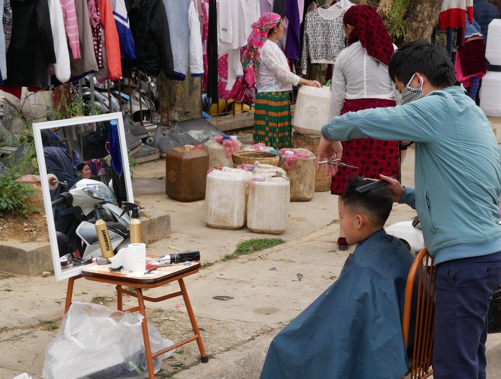 A young boy looks at his reflection as he has his hair cut in a makeshift salon on the street