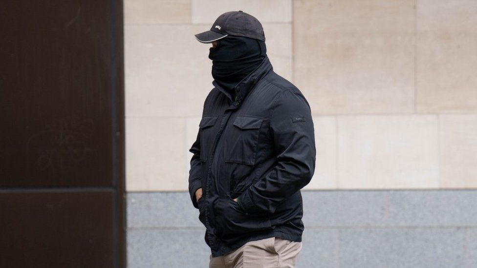 Thomas Phillips arrives at Westminster Magistrates Court wearing a balaclava, baseball cap and black coat