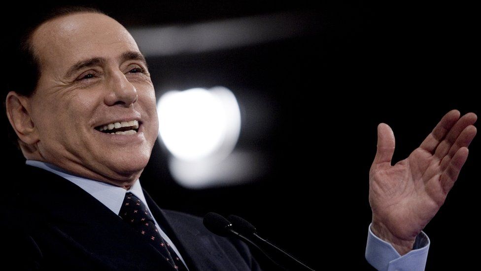 Берлускони улыбается и жестикулирует открытой ладонью на этой фотографии крупным планом 2010 года