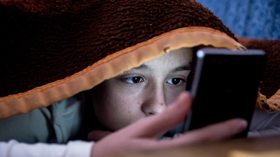 Child looking at mobile phone in bed