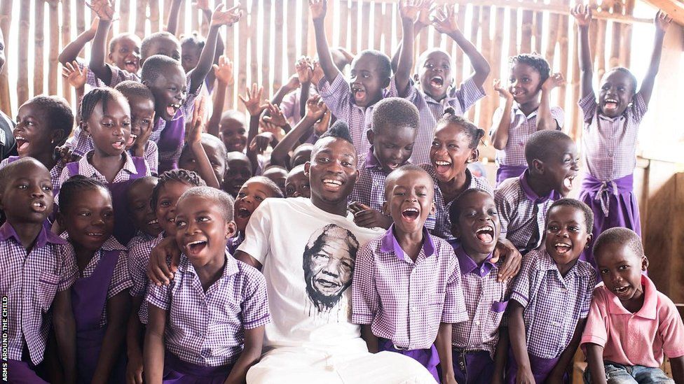 Christian Atsu surrounded by smiling children in a classroom