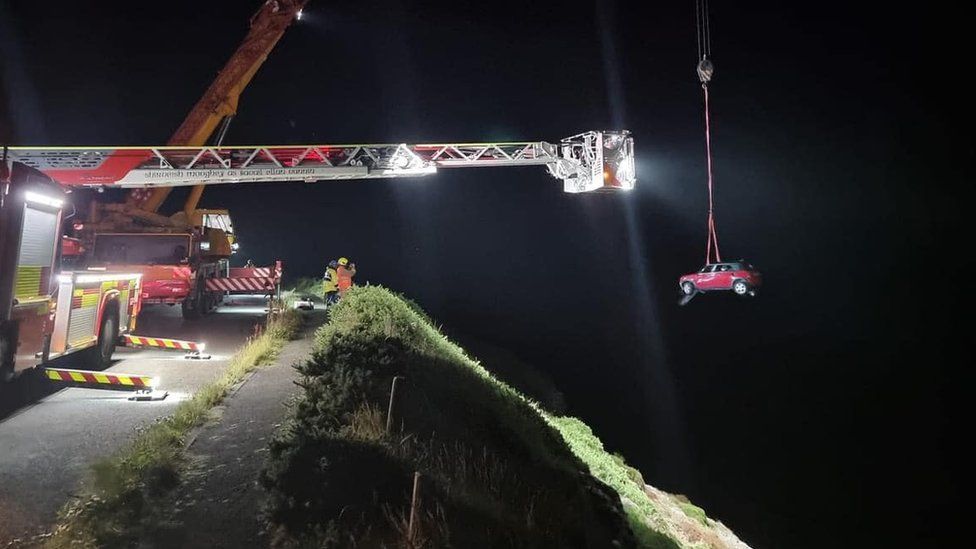 Car hanging from a crane above the cliff edge
