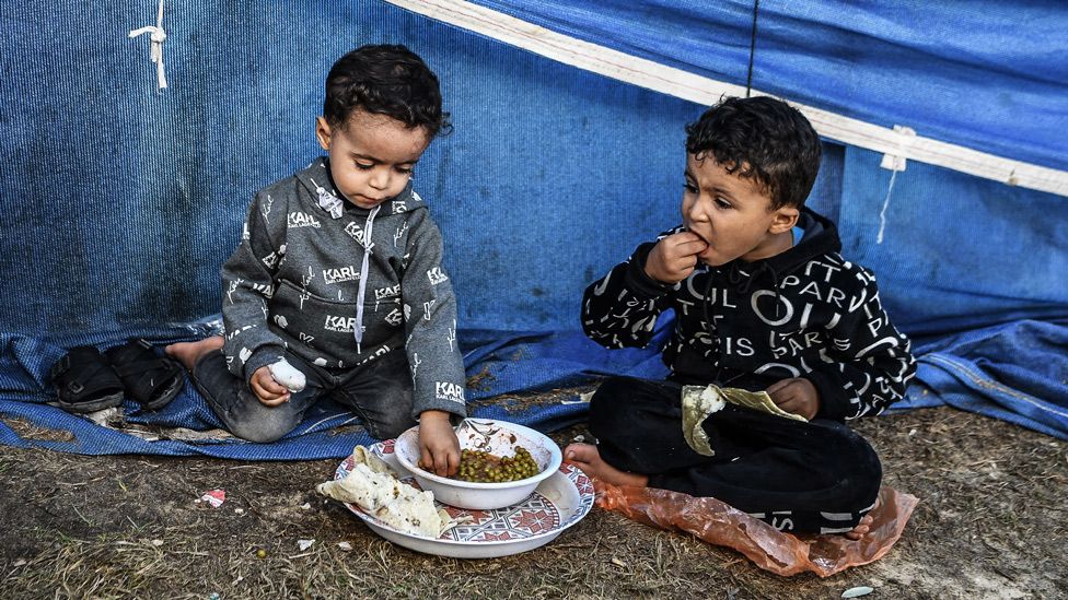 Palestinian children, who were displaced to the area around Nasser Hospital in Khan Yunis, eat food distributed by volunteers - 21 November 2023