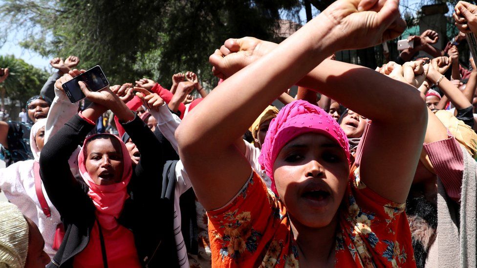 Women supporters show the Oromo protest gesture outside Jawar Mohammed's house