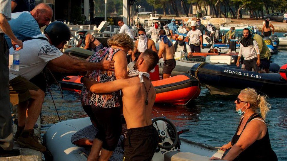 Люди эвакуируются на лодках во время лесного пожара в Неа-Анхиалосе, недалеко от Волоса, Греция 27 июля 202