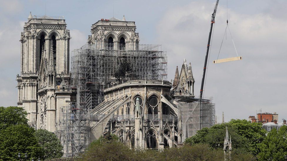 Fire fighters are at work on top of a tower of Notre-Dame Cathedral, as a crane lifts up constreuction material in Paris on April 17, 2019,