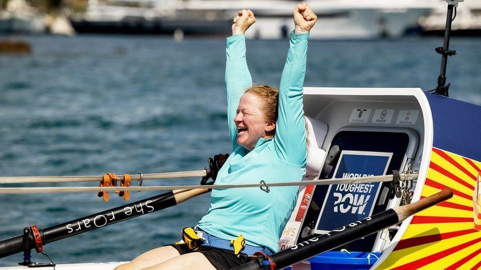 Leanne in her boat raising her arms in celebration