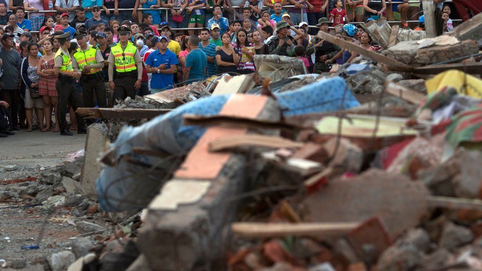 Residents look at rescue workers toil in an earthquake collapsed building in Manta, Ecuador.