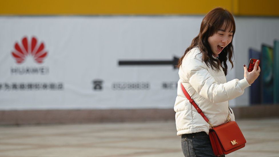 A woman laughs while using her smartphone outside a Huawei store in Beijing on January 29, 2019
