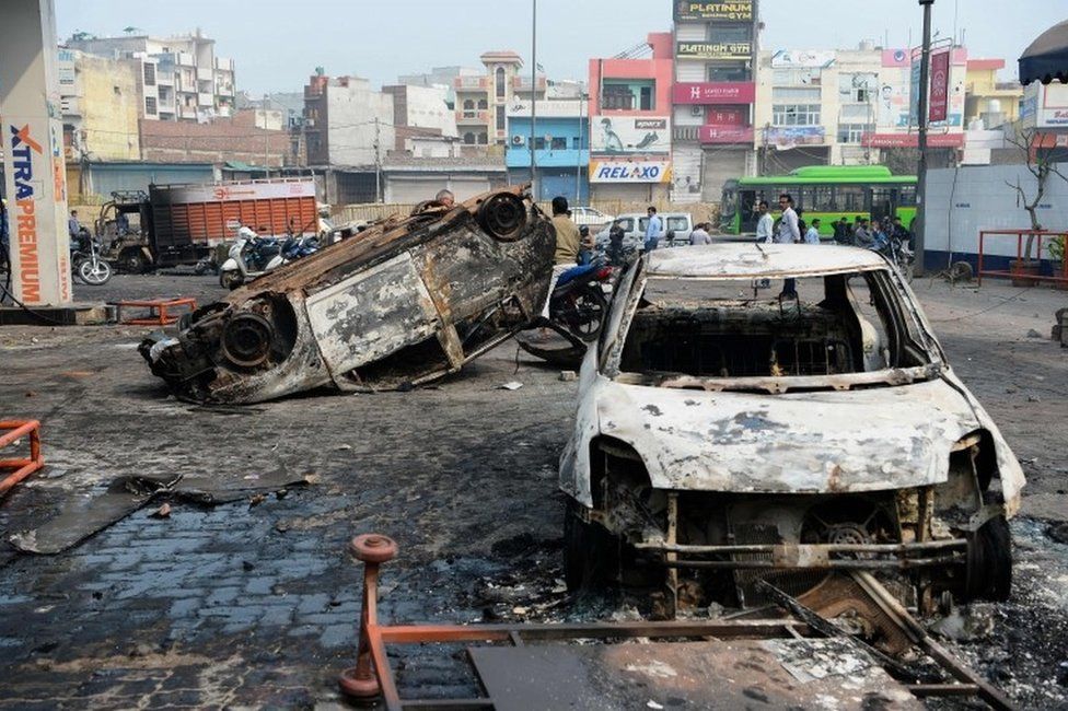 Local residents look at burnt-out vehicles following clashes between people supporting and opposing a contentious amendment to India"s citizenship law, in New Delhi on February 26, 2020