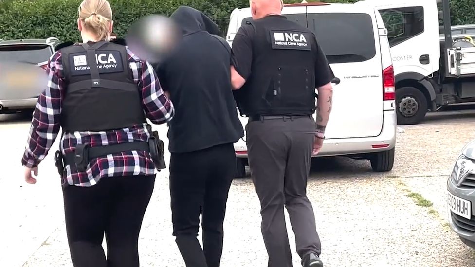 A man is seen being led away in handcuffs following a raid by the National Crime Agency targeting suspected people smugglers in London on 12 July 2022