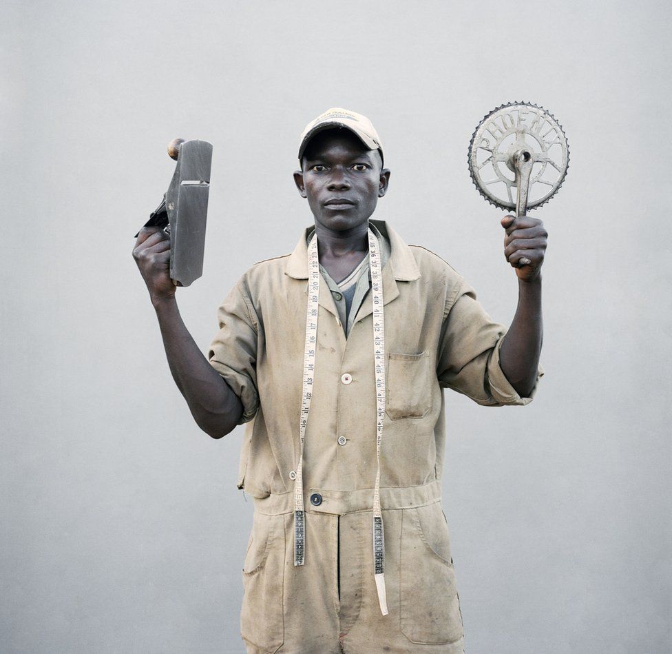 A young man holds up his tools.
