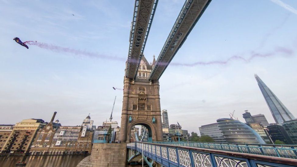 Marco Fürst and Marco Waltenspiel fly past the top section of Tower Bridge in London in their wingsuits, leaving behind red smoke trails