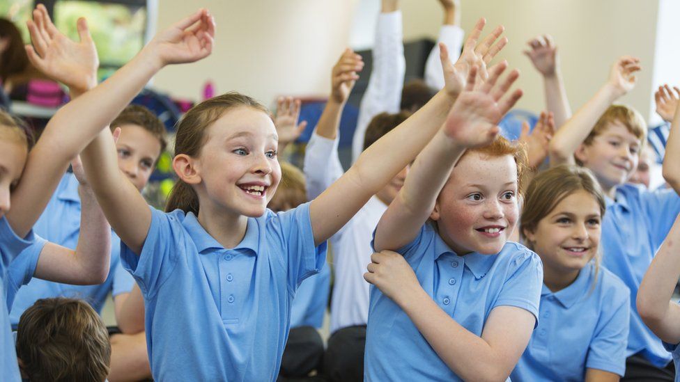 Children putting their hands up to answer questions in a classroom