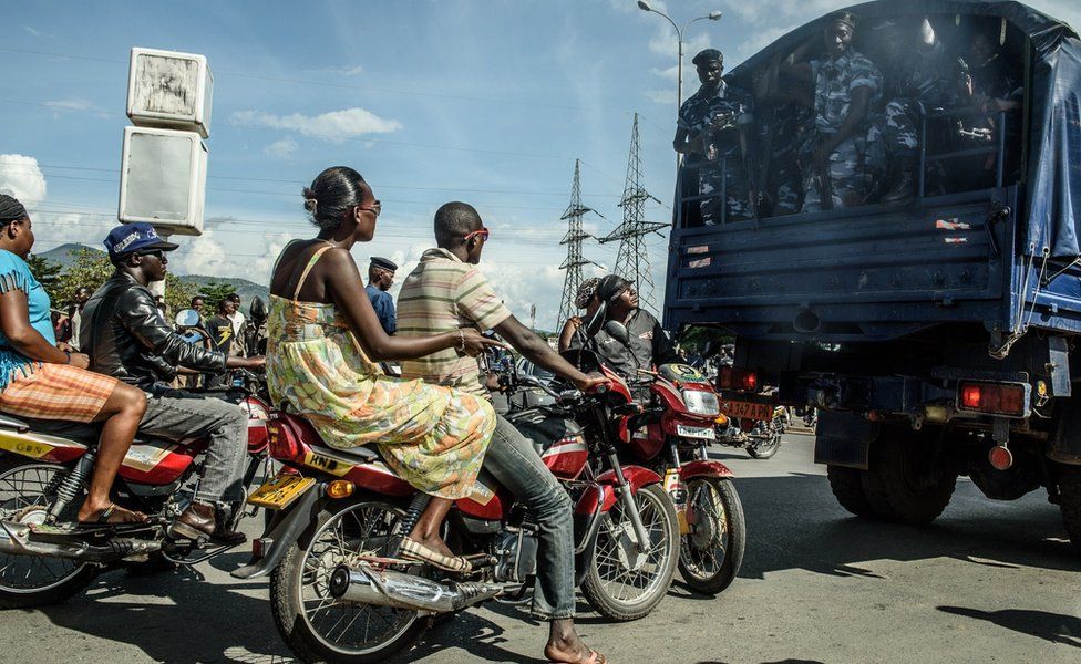 People ride motorbikes behind a truck transporting security forces in Bujumbura on 15 May 2015