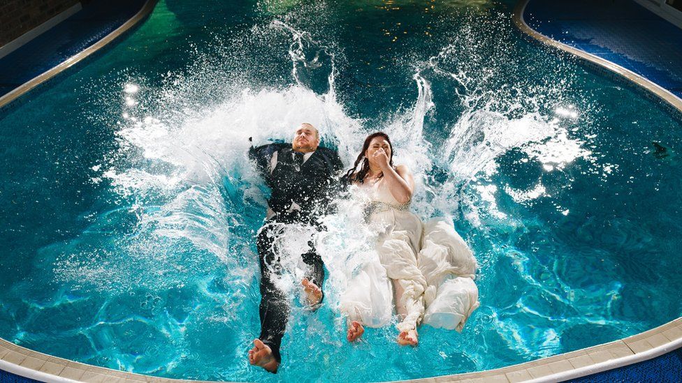Louise Young and Sam Gilbert jumping into a swimming pool on their wedding day