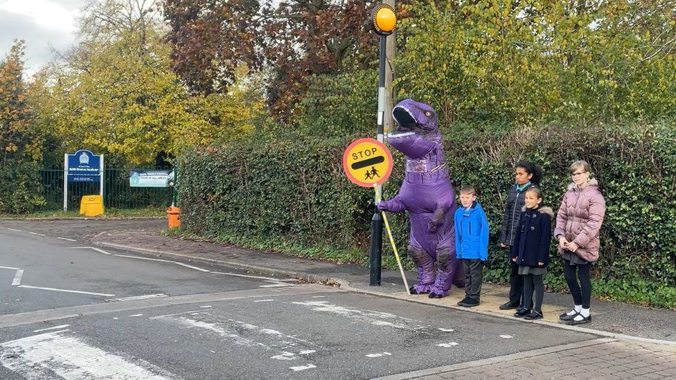 Eight foot purple dinosaur on patrol helping children cross a road in Edith Weston, Rutland
