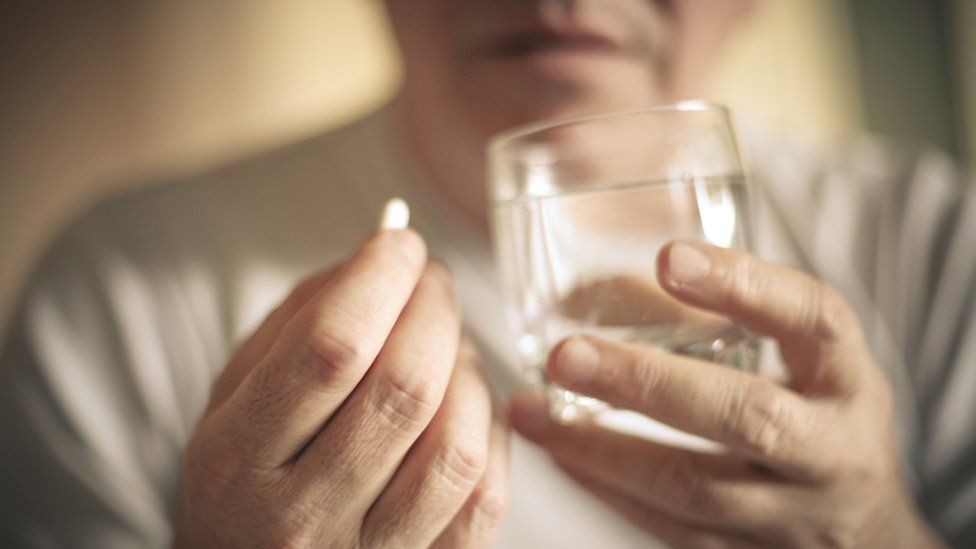 A woman holds a painkiller pill and a glass of water