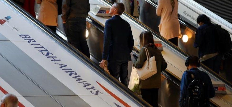 People on escalator passing BA logo
