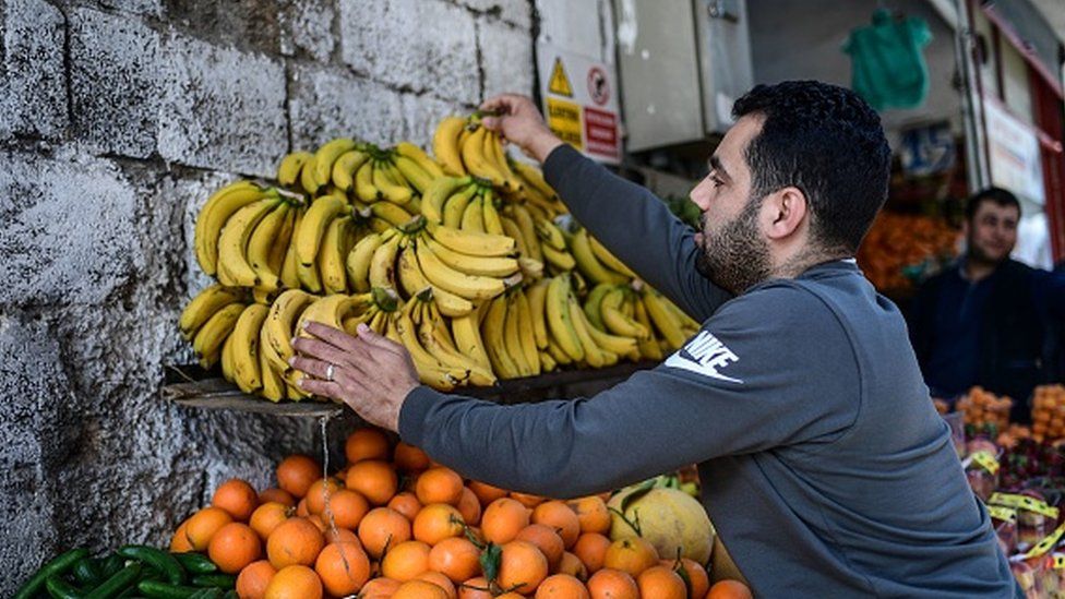 Сирийский овощной торговец демонстрирует бананы на прилавке своего магазина в Газиантепе
