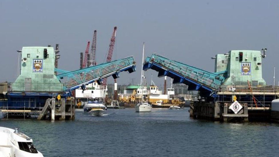 The two sections of Poole Bridge raising with a motorboat and a sail boat approaching to travel through the opening