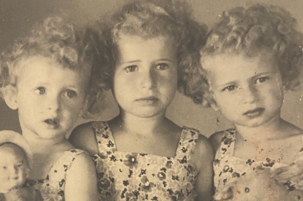 Three young girls with blond curly hair look at the camera