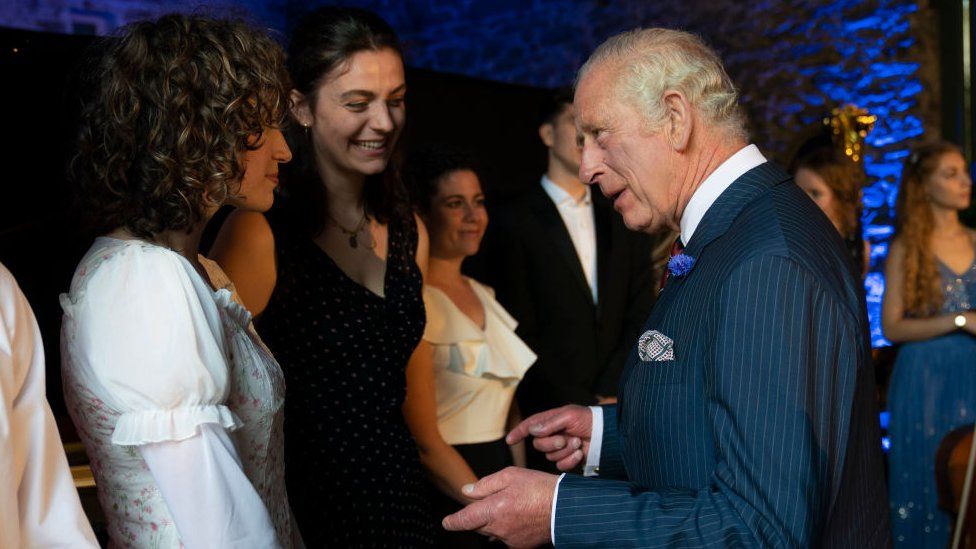 Prince Charles in a reception chatting intently with women in fancy gowns