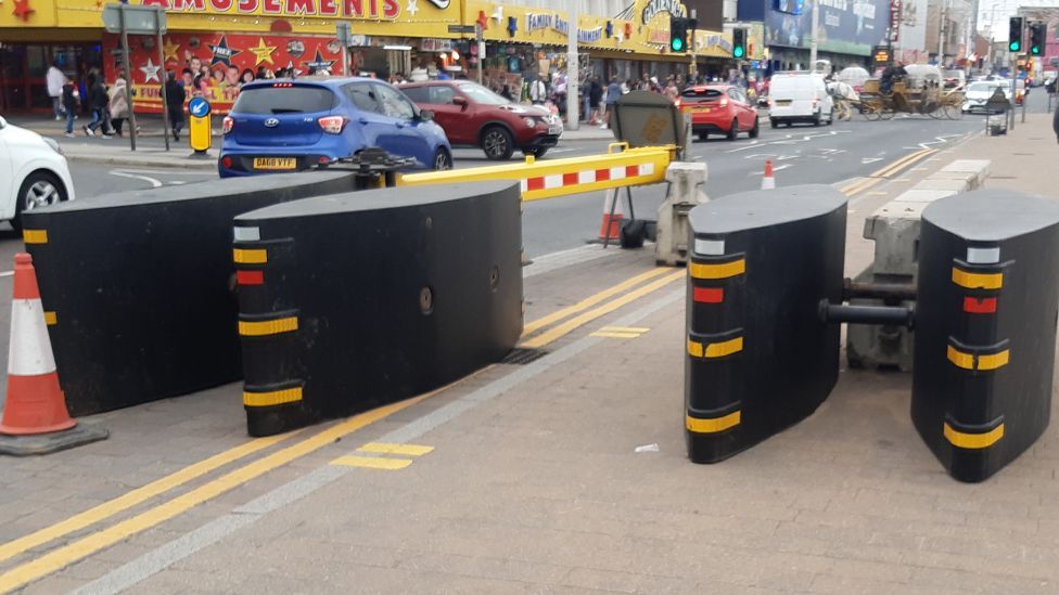 Large, heavy, black oval shaped barriers with reflective tape by the side of the road on the Promenade