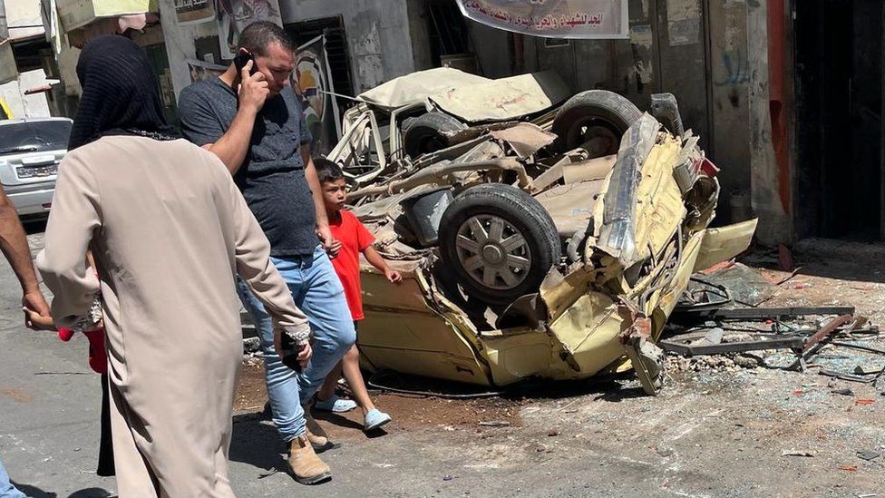 Palestinians walks past   a damaged and overturned car   successful  Jenin exile  camp, successful  the occupied West Bank, pursuing  a large   Israeli subject   cognition  (5 July 2023)