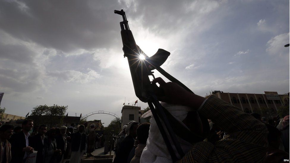 An armed Houthi supporter holds up guns during a protest