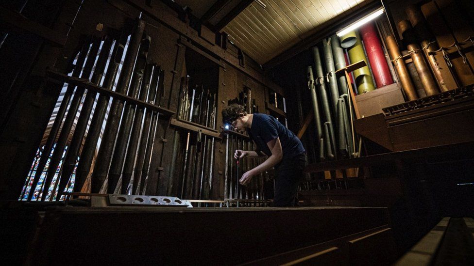 Image of a man working on the organ in Gloucester Cathedral. He is wearing a head lamp.