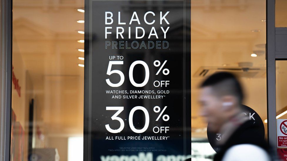 A man walks past a shop window in which is displayed a Black Friday offer.