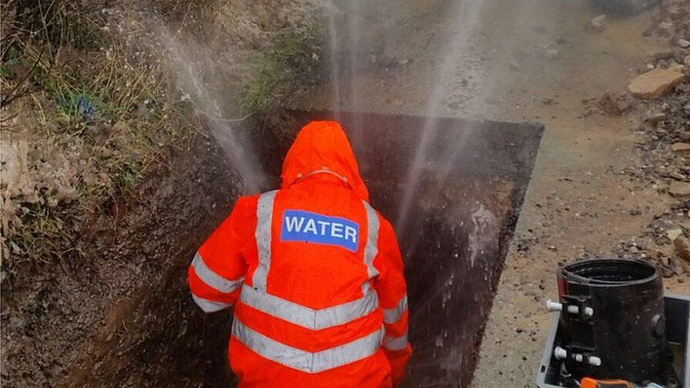 A Severn Trent engineer fixing a burst pipe as water sprays into the air