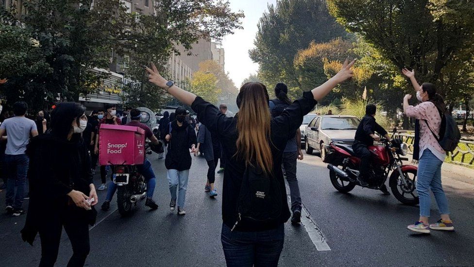 Protesters, including a woman with uncovered hair, block a road during a protest over the death in custody of Mahsa Amini, in Tehran, Iran (1 October 2022)