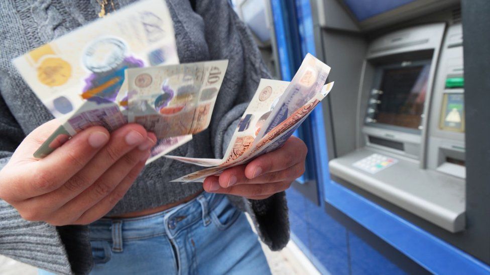 Женщина достает деньги из банкомата