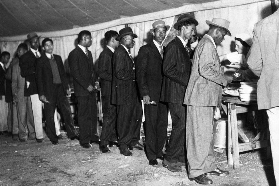 Jamaican men in Britain to look for work, line up in a canteen marquee to get a meal, 1948